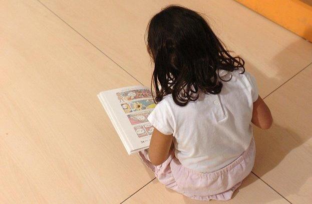 Una niña lee un libro en una biblioteca infantil.