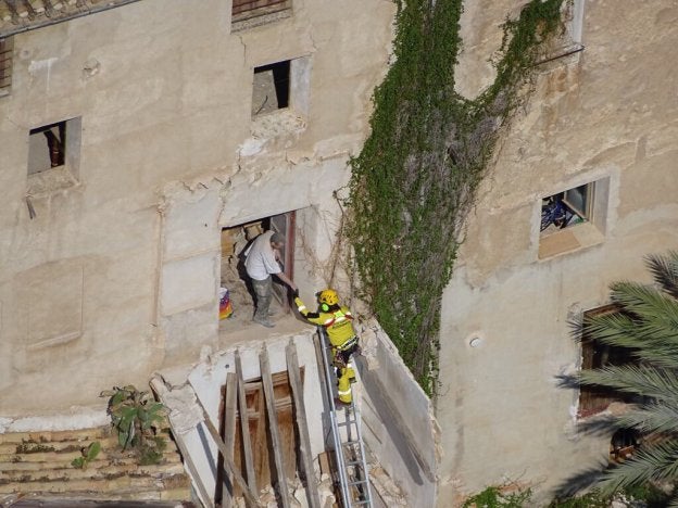 Un bombero ayuda a la víctima que quedó atrapada tras el derrumbe, junto a la fachada al descubierto.