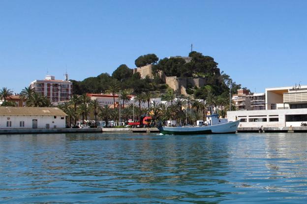 El castillo de Dénia, cubierto en gran parte de árboles, visto desde la zona portuaria de la ciudad. / Tino Calvo